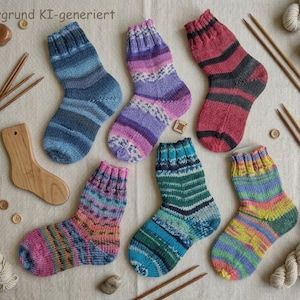 Könnte beinhalten: Sechs handgestrickte Wollsocken mit verschiedenen mehrfarbigen Streifenmustern in Blau-, Lila-, Rot-, Rosa- und Grüntönen. Das Set enthält Stricknadeln aus Holz, kleine Holzknöpfe und eine Sockenform aus Holz auf einem textilen Untergrund.