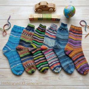 Könnte beinhalten: Sechs Paar handgestrickte Wollsocken mit verschiedenen bunten Streifenmustern, in einer Reihe angeordnet. Darüber befinden sich ein Holzspielzeugauto, ein Satz Buchstabenwürfel, die ein Wort bilden, und ein kleiner bunter Globus.