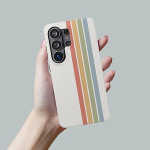 May include: A white phone case with a vertical stripe design in red, orange, yellow, green, and blue. The case has a camera cutout and is held in a hand.