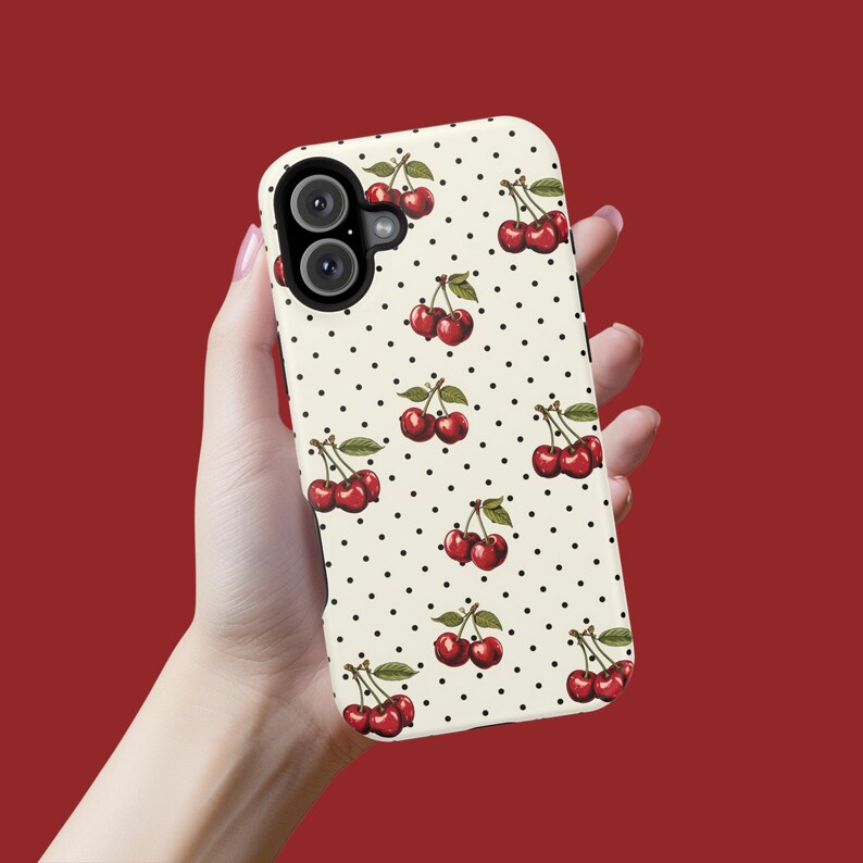 May include: A white phone case with a pattern of red cherries and black polka dots. The case has a dual camera lens.