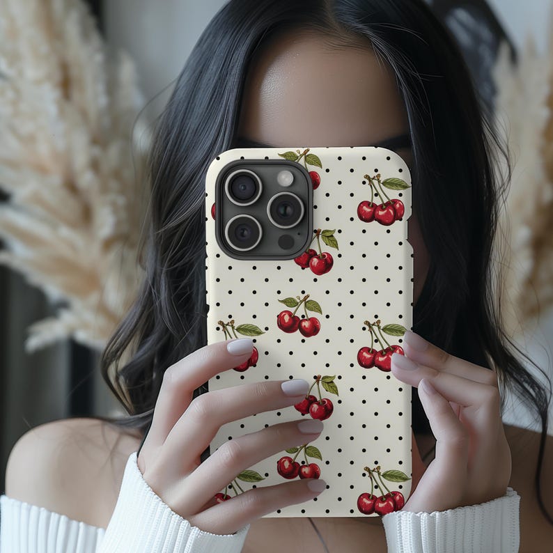 May include: A white phone case with a black polka dot pattern and a red cherry design. The case has a camera lens cutout and a white background.
