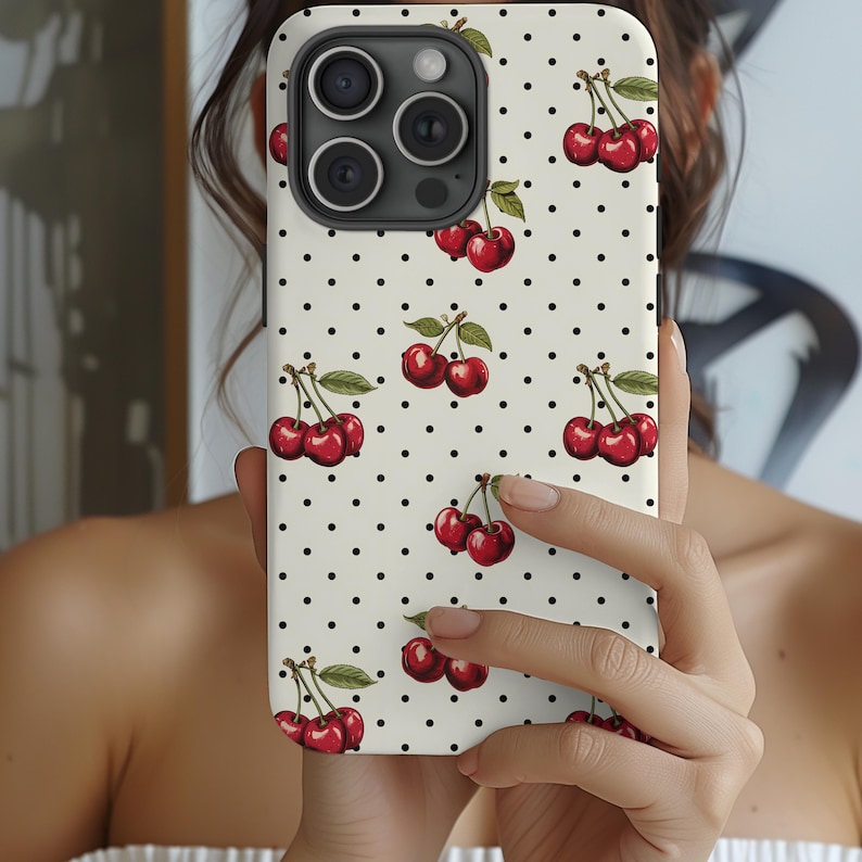 May include: A white phone case with a black polka dot pattern and a red cherry design. The case has a camera lens cutout and a cutout for the phone's buttons.