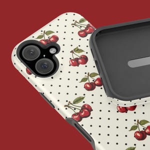 May include: A white phone case with a pattern of red cherries and black polka dots. The case has a raised camera bump with two lenses.
