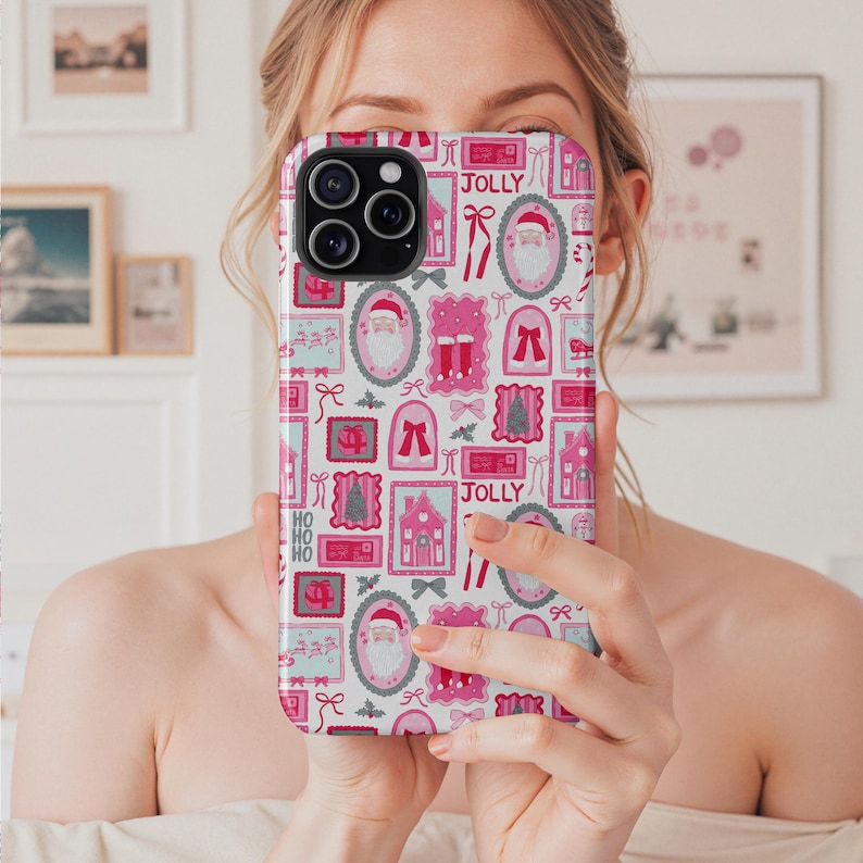May include: A phone case with a festive Christmas pattern. The design features pink and white frames with images of Santa Claus, bows, houses, and the word "JOLLY". The case has a black camera module.