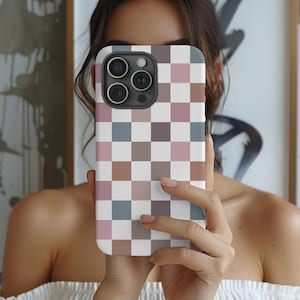 May include: A white phone case with a checkered pattern in shades of pink, brown, and blue. The case has a raised camera bump with three lenses.