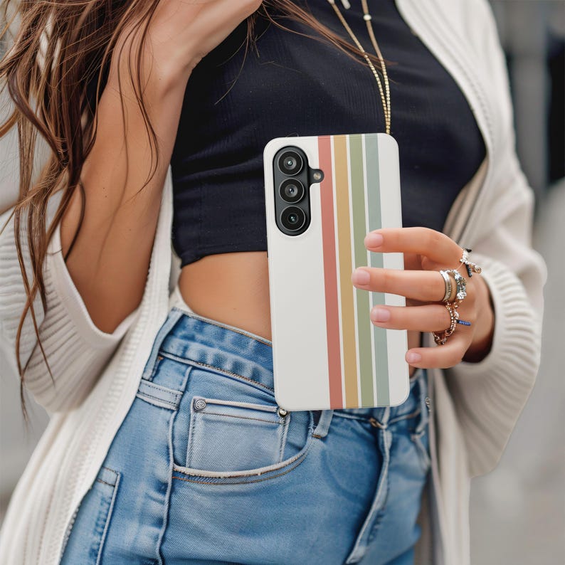 May include: A white smartphone case with vertical stripes in muted colors of red, yellow, green, and brown. The phone case has a camera on the upper left side. The case is being held.