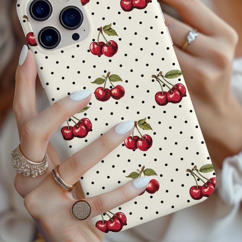 May include: A white iPhone case with a black polka dot pattern and a repeated design of red cherries with green stems and leaves.