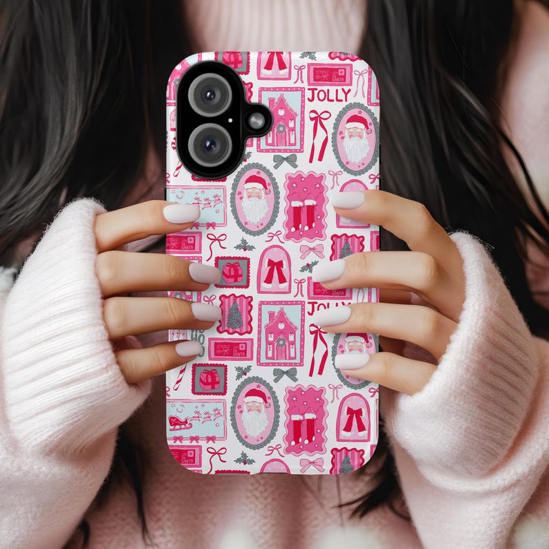 May include: A pink and white phone case featuring a festive Christmas design. The case is covered in illustrations of Santa Claus, houses, bows, and the word "JOLLY". The case is held by a person wearing a pink sweater.