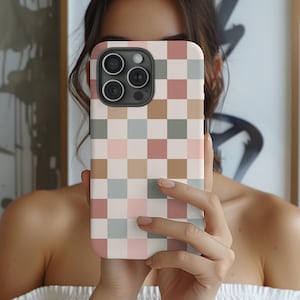 May include: A white phone case with a checkered pattern in shades of pink, brown, and green. The case has a camera lens cutout.