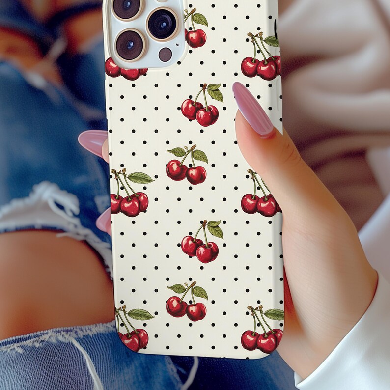 May include: A white phone case with a black polka dot pattern and a repeating pattern of red cherries. The case is designed for a smartphone with a camera bump.