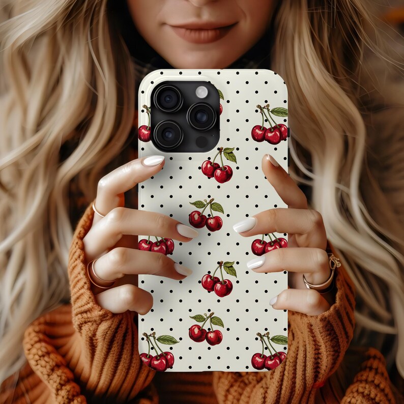 May include: A white phone case with a black polka dot pattern and a repeating image of red cherries. The case has a camera lens cutout with three black circles.