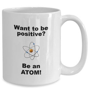 May include: White ceramic mug with a black and white graphic of an atom and the text "Want to be positive? Be an ATOM!"