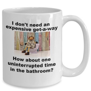 May include: White ceramic coffee mug with a humorous saying about needing a bathroom break instead of an expensive holiday. The mug features a cartoon illustration of a sheep sitting on a toilet.
