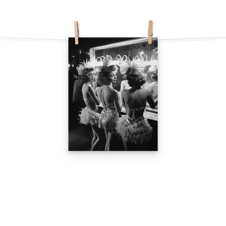 May include: Three women in feather boas and sequined costumes stand in front of a mirror in a dressing room. They are looking at their reflections and adjusting their outfits.