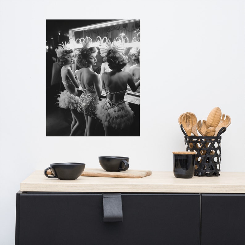 May include: Three women in feathered headdresses and costumes stand in front of a mirror, looking at their reflections. The image is in black and white.