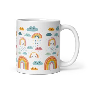 Pode incluir: Caneca de cerâmica branca com um padrão repetido de arco-íris coloridos, nuvens sorridentes e gotas de chuva. Os arco-íris são laranja, amarelo e rosa. As nuvens são azuis, rosa e laranja. A caneca tem uma alça branca.