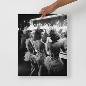May include: Three women in black and white, wearing feather boas and sequined costumes, stand in front of a mirror in a dressing room. They are looking at their reflections.