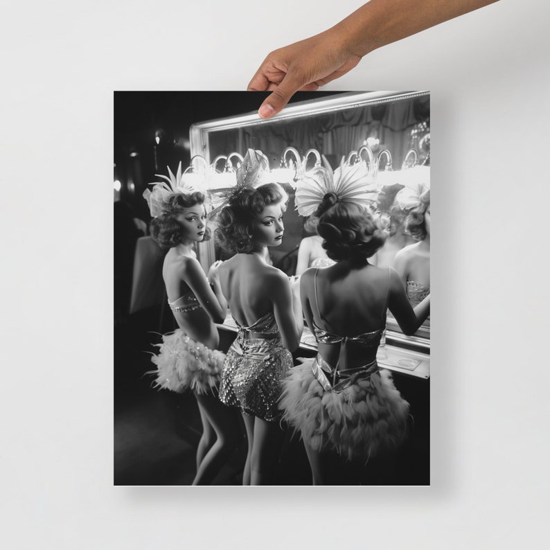 May include: Three women in black and white, wearing feather boas and sequined costumes, stand in front of a mirror in a dressing room. They are looking at their reflections.