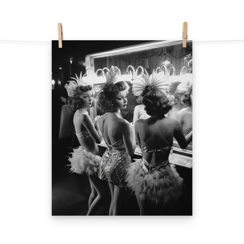 May include: Three women in black and white, wearing feathered costumes and headpieces, stand in front of a mirror, looking at their reflections.