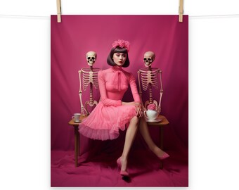 May include: A woman in a pink dress sits at a table with two skeletons. She is holding a teacup and saucer. The skeletons are wearing pink flowers on their heads. The background is a solid pink.
