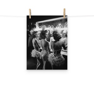 May include: Three women in feather boas and sequined costumes stand in front of a mirror in a dressing room. They are looking at their reflections and adjusting their costumes.