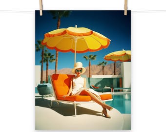 May include: A retro-style print showing a woman in a white dress and hat, seated on an orange sun lounger under a yellow and orange parasol. Palm trees and a pool are in the background, with a clear blue sky.