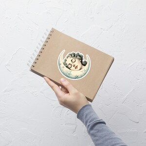 May include: A sticker featuring a vintage illustration of a woman sleeping inside a crescent moon with stars. The moon is white with a blue and green gradient.