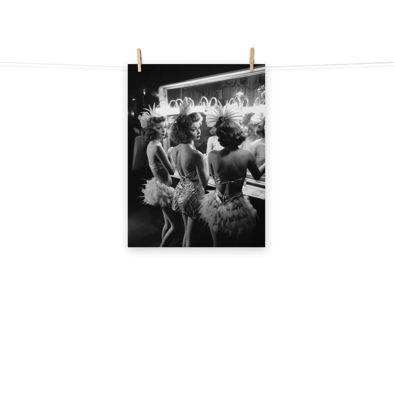 May include: Three women in black and white, wearing feathered and sequined costumes, stand in front of a mirror in a dressing room. They are looking at their reflections.