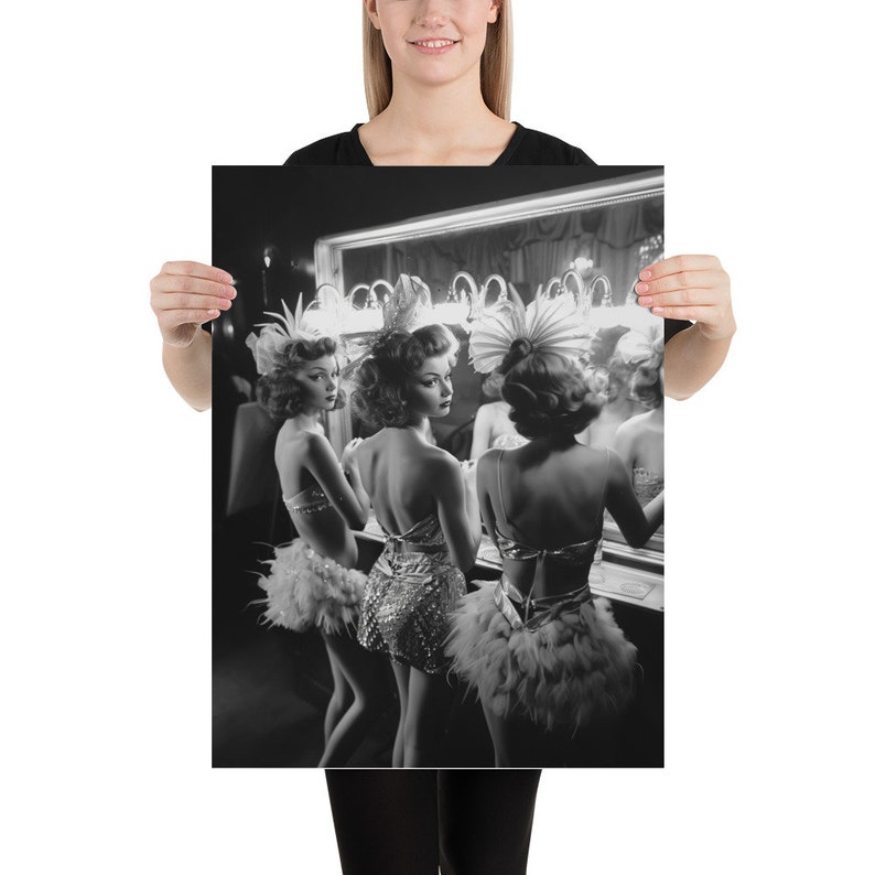 May include: Three women in black and white, wearing feathered headdresses and sequined costumes, stand in front of a mirror in a dressing room.