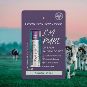 Puede incluir: Una tarjeta morada con un tubo de bálsamo labial con la inscripción "I'M PURE" y el texto "Ancestral Dream". La tarjeta también indica "100% de origen animal", "cuidado mínimo de la piel", "sin microplásticos" y "cero residuos". Dos vacas pastan en un campo verde al fondo.