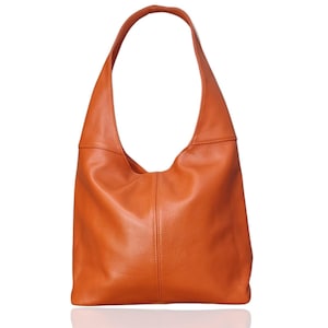 May include: An orange leather shoulder bag with a single strap. The bag has a rounded shape and a smooth texture. The bag is sitting on a white surface.
