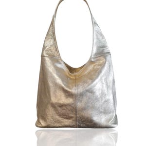 Puede incluir: Un bolso hobo de cuero plateado con una sola correa. El bolso tiene un aspecto informal y holgado.