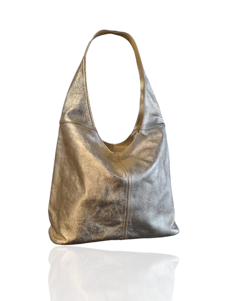 Puede incluir: Un bolso hobo de cuero met&aacute;lico plateado con una sola correa. El bolso tiene un aspecto informal y holgado.