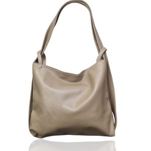 May include: A beige leather shoulder bag with a soft, slouchy design. The bag has long straps and a simple, elegant shape. The leather appears to be smooth and has a slight sheen. The bag is shown against a white background.
