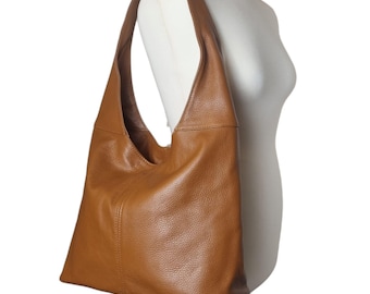 May include: A brown leather shoulder bag with a large, open design. The bag is a warm, medium brown color and has a soft, textured appearance. The strap is wide and comfortable, designed to be worn over the shoulder. The bag is displayed on a white mannequin.