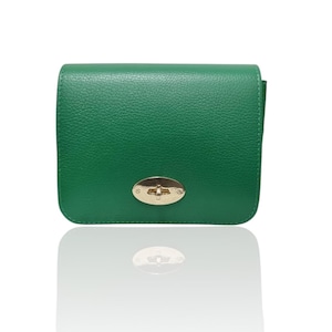 Puede incluir: Un pequeño bolso de mano de cuero verde esmeralda con un cierre dorado. El bolso tiene forma rectangular con bordes redondeados y una superficie texturizada. El cierre es de forma ovalada con un diseño decorativo.