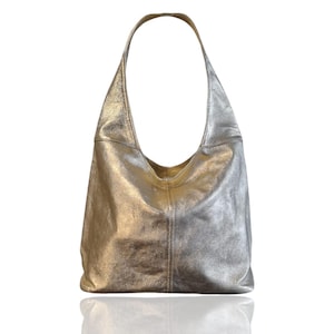 Puede incluir: Un bolso hobo de cuero plateado con una sola correa.