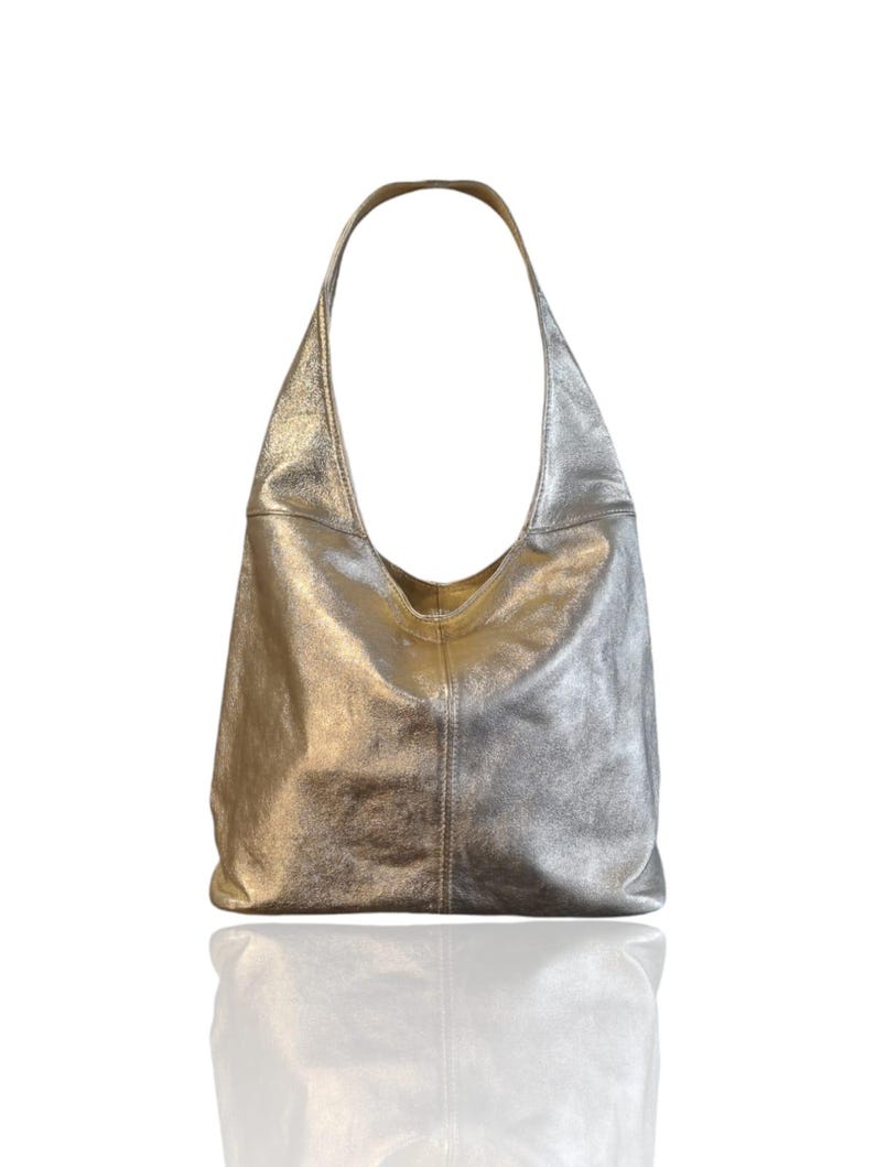 Puede incluir: Un bolso hobo de cuero plateado con una sola correa.