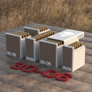 May include: A display of ammunition boxes, each filled with brass-cased bullets. The boxes are brown and white, labeled "30-06" and "3006". A red "30-06" is placed in front. One box has a skull logo.