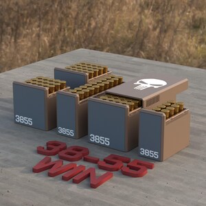 May include: Four brown and gray ammunition boxes filled with brass-colored bullets. The boxes are labeled "3855" and arranged on a concrete surface. The text "38-55 WIN" is in red, three-dimensional letters.
