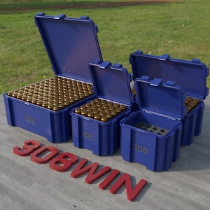 May include: Several blue storage containers filled with brass-colored ammunition. The containers are open, revealing the contents. The text "308" is printed on the side of each container. The red text "308WIN" is on the ground.