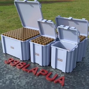 May include: Several light blue storage containers with open lids, filled with numerous brass-colored objects. The containers are labeled "338" and are arranged on a textured surface. Red letters spell out "338 LAPUA" in the foreground.