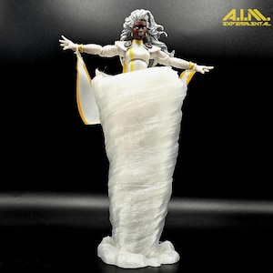 May include: A white action figure of Storm from the X-Men, with silver hair and a white and yellow costume. The figure is posed with arms outstretched, standing on a swirling white cloud base. The logo "A.I.M. EXPERIMENTAL" is in the upper right corner.