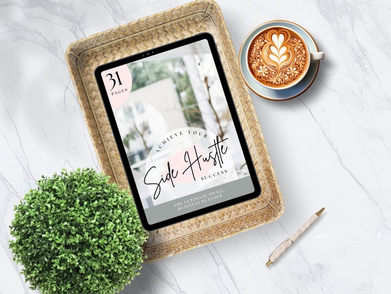 Puede incluir: Una tableta mostrando un planificador digital con el texto "Achieve Your Side Hustle Success" y "The Ultimate Small Business Planner". La tableta est&aacute; en una cesta tejida sobre una superficie de m&aacute;rmol blanco con una taza de caf&eacute; y un bol&iacute;grafo.