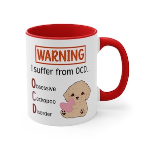 Peut inclure: Une tasse en céramique blanche avec un bord et une poignée rouges. La tasse porte une pancarte d'avertissement qui dit "ATTENTION Je souffre de TOC... Obsession Cockapoo Trouble" avec une image de dessin animé d'un cockapoo brun tenant un cœur rose.