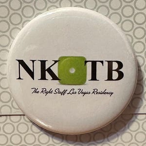 May include: A white button with the text "NKOTB" in black, a green square with a white dot, and the text "The Right Stuff Las Vegas Residency" in black. The button has a glossy finish.