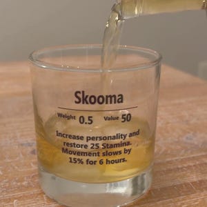 May include: A glass of Skooma, a fictional alcoholic beverage from the video game The Elder Scrolls, being poured from a bottle. The glass has a label that reads "Skooma", "Weight 0.5", "Value 50", "Increase personality and restore 25 Stamina. Movement slows by 15% for 6 hours."