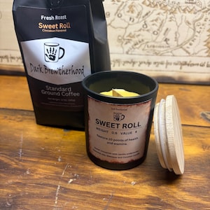 May include: A black and brown coffee bag with the text "Fresh Roast Sweet Roll Cinnabun Flavored Dark Brewtherhood Standard Ground Coffee". A black candle with a wooden wick and a white lid. The candle has the text "Sweet Roll Weight 0.6 Value 4 Restore 10 points of health and stamina. Sweet cinnamon with vanilla undertones. Essential Oils:  Bergamot and Coconut Candy."