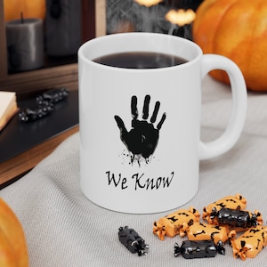 May include: White ceramic coffee mug with a black handprint and the text "We Know".