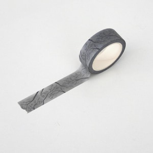 Puede incluir: Un rollo de cinta adhesiva washi gris con un diseño de ramas de árbol. La cinta está desenrollada, mostrando el diseño. El fondo es blanco.